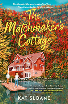 A couple stands on a dock by a large lakeside cottage, surrounded by autumn trees. Book title: The Matchmaker’s Cottage.