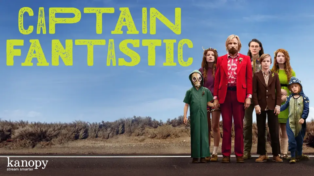 A man in a red suit stands with six children in front of a road, under the title "Captain Fantastic.