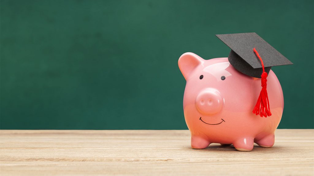 Piggy bank wearing a graduation cap on a wooden surface with a green background.