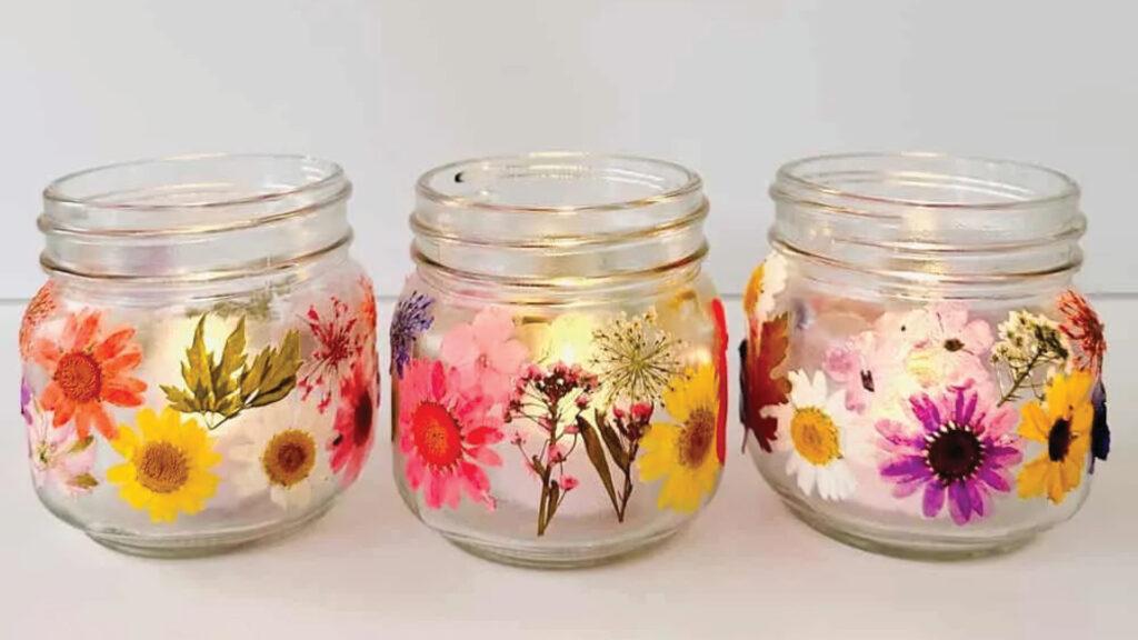 Three glass jars decorated with colorful pressed flowers and leaves, arranged side by side on a white surface.