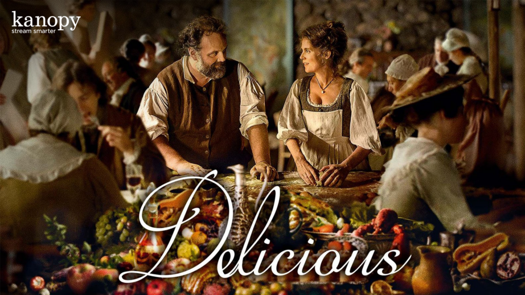 A man and woman prepare food together in a busy, rustic kitchen; "Delicious" is written across the image.