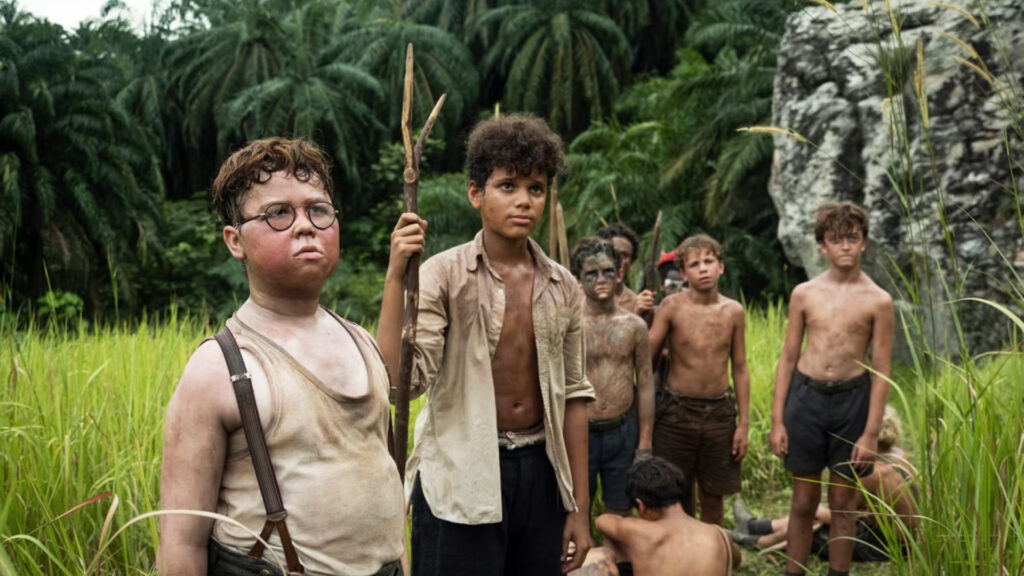 A group of dirty, shirtless boys stand in tall grass in front of palm trees, looking serious and alert.