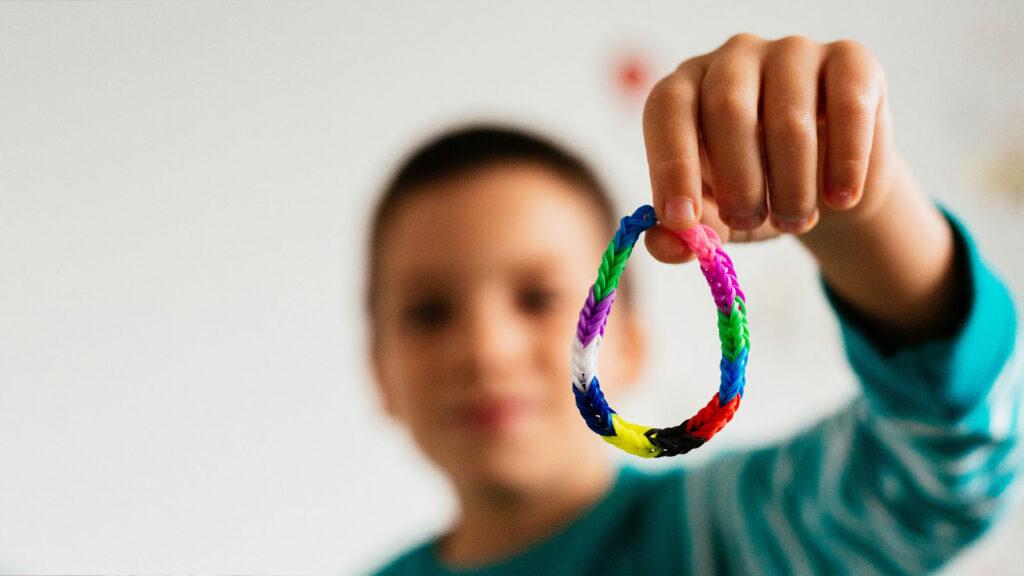 A child in a blue shirt holds up a colorful woven bracelet toward the camera.