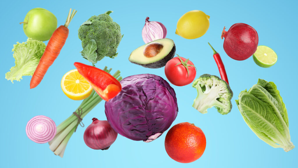 Various colorful fruits and vegetables floating on a blue background, including cabbage and avocado.