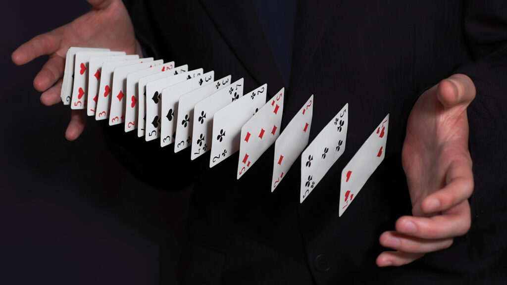 A person in a suit performing a card flourish, spreading playing cards between both hands.