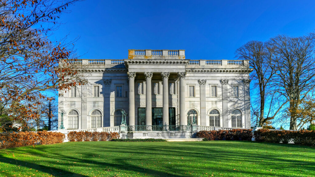 White neoclassical mansion with tall columns and arched windows, surrounded by trees and green lawn.