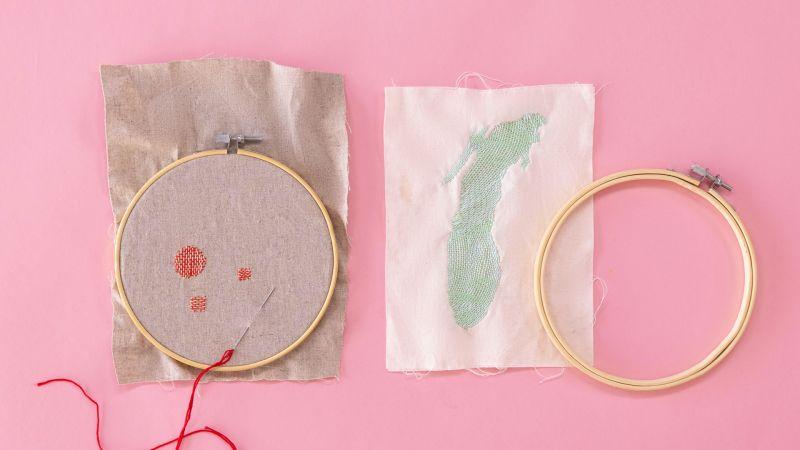 Two embroidery hoops on fabric with red and green stitching, placed on a pink background.