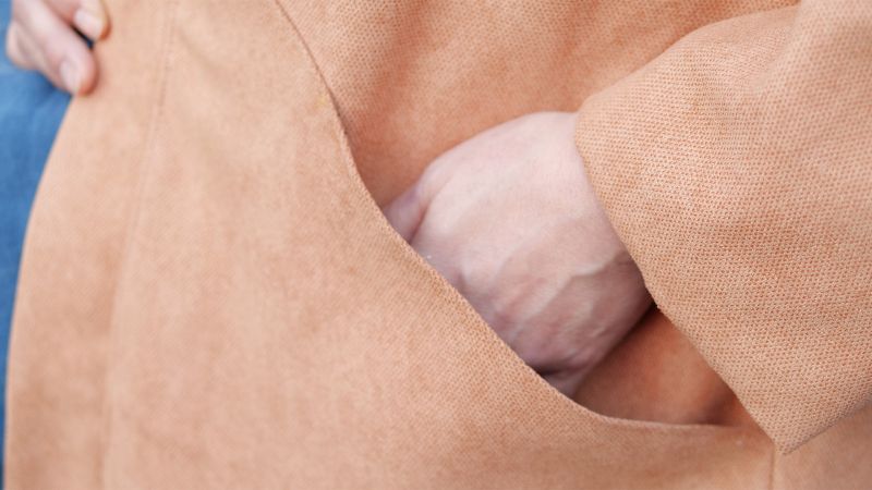 A hand is placed inside the pocket of a tan coat.