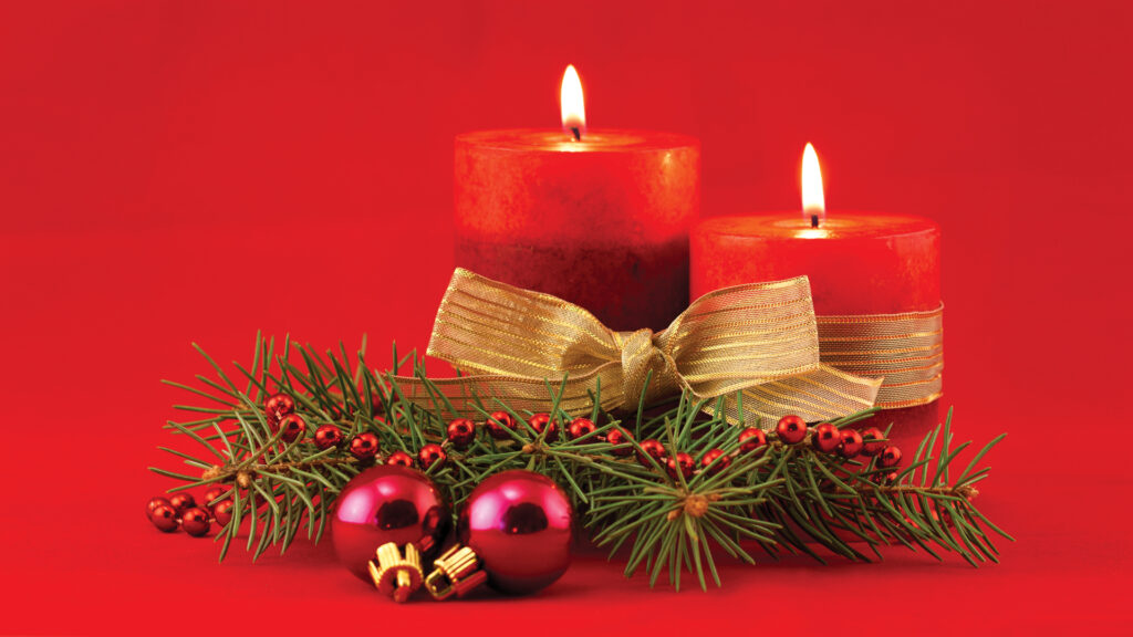 Two red candles with gold ribbon, pine branches, and red ornaments on a red background.