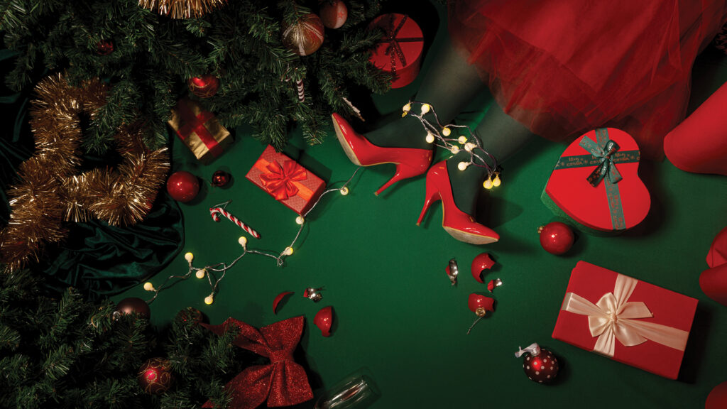 Woman in red heels under a Christmas tree, surrounded by gifts, ornaments, lights, and festive decor.