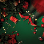 Woman in red heels under a Christmas tree, surrounded by gifts, ornaments, lights, and festive decor.