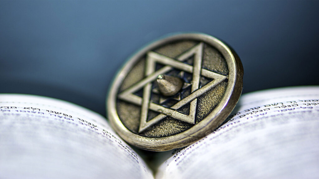 Star of David pendant resting on an open book with Hebrew text.