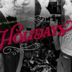 An older man and a woman smile and toast drinks by a Christmas tree, with "Holidays" in festive text.