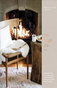 Cozy seating with a blanket and coffee by a fireplace, featuring the text "the hygge life" on the book cover.