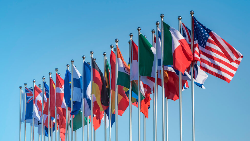 A row of international flags waving against a clear blue sky.