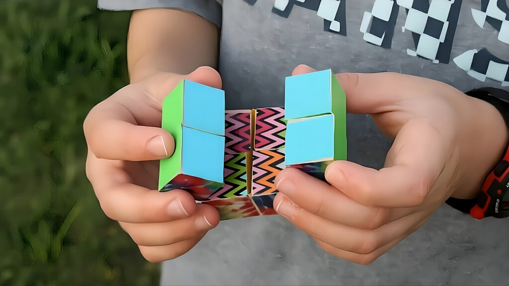 Child holding a colorful geometric fidget toy with both hands, outdoors, wearing a gray shirt.