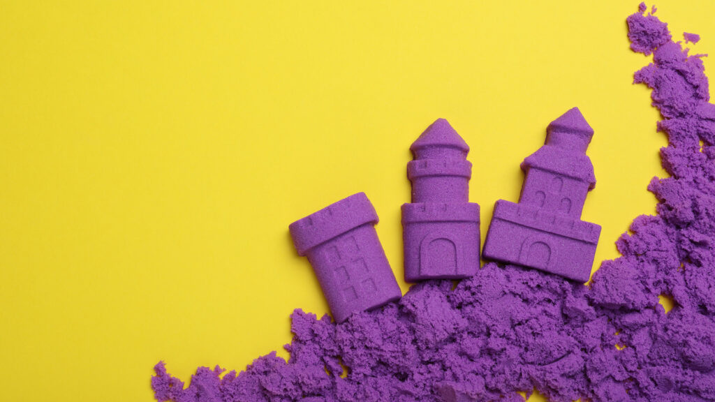 Three purple toy sandcastles on yellow background with scattered purple sand.