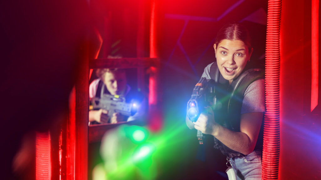 Two people playing laser tag, aiming toy laser guns in a dark, neon-lit arena with colorful lights.