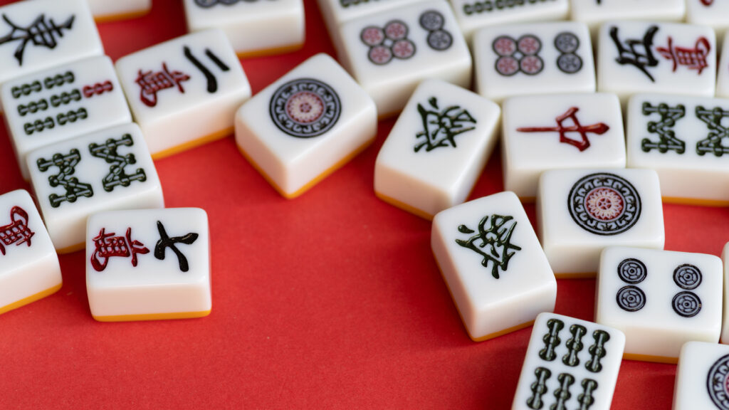 Mahjong tiles with various symbols are scattered on a red surface.