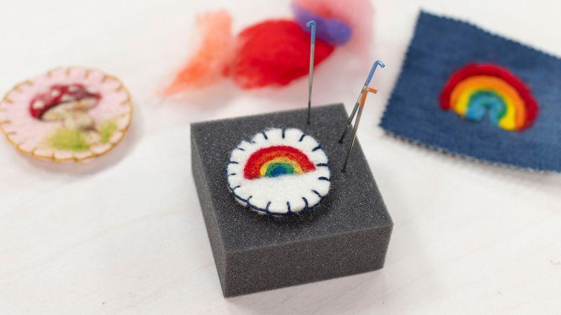 Colorful felt patches on a foam block, featuring a rainbow design, with felting needles inserted.