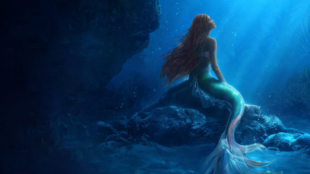 A mermaid with long red hair sits on a rock underwater, gazing up at the light filtering through the sea.