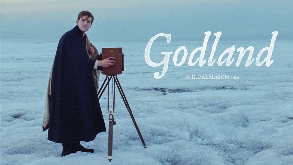 A person in a cape stands on ice with an old camera; text reads "Godland, an H. Pálmason film.