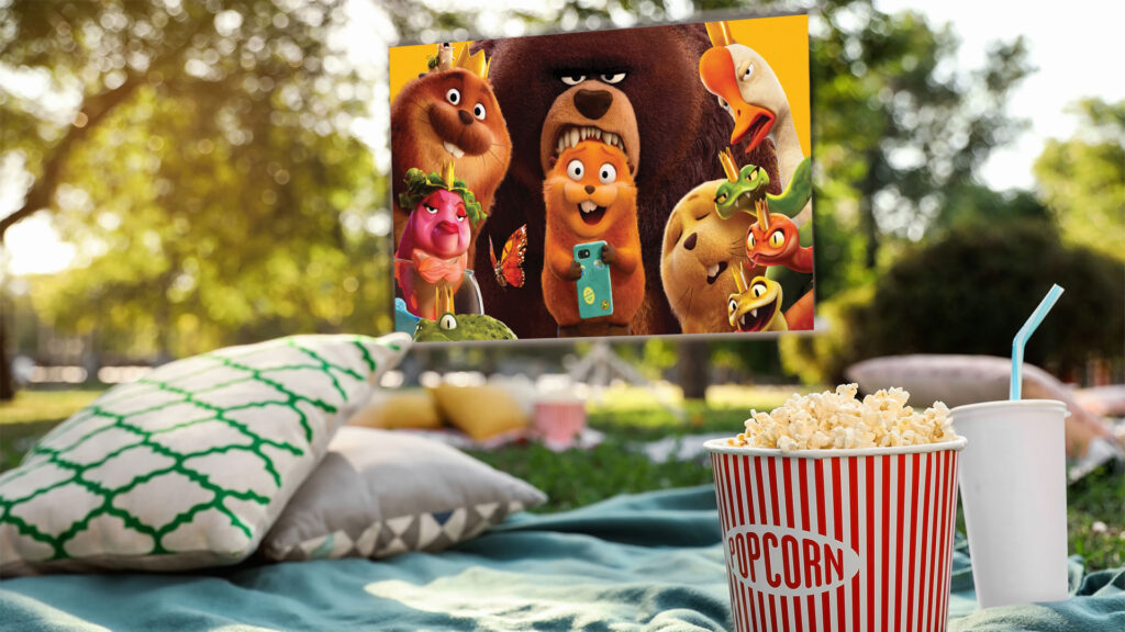 Outdoor movie night with popcorn, drinks, and animated animal film playing on a screen in a park setting.