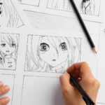 A person draws manga characters with large eyes on comic panels using a black pen on a white desk.