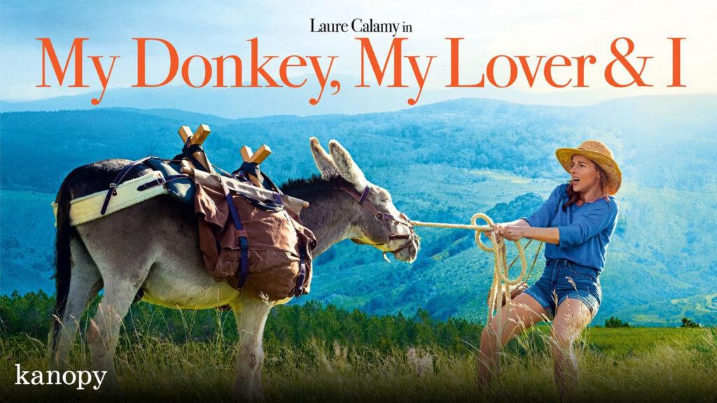 A woman in a hat playfully pulls a rope tied to a donkey in a scenic mountain landscape.