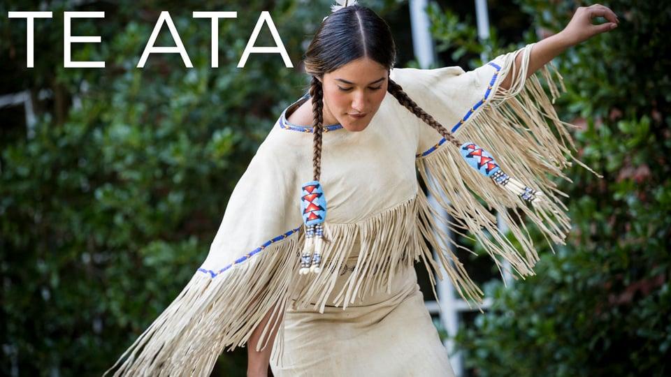 Person dancing in traditional attire with fringe, against a backdrop of green foliage. Text reads "TE ATA".