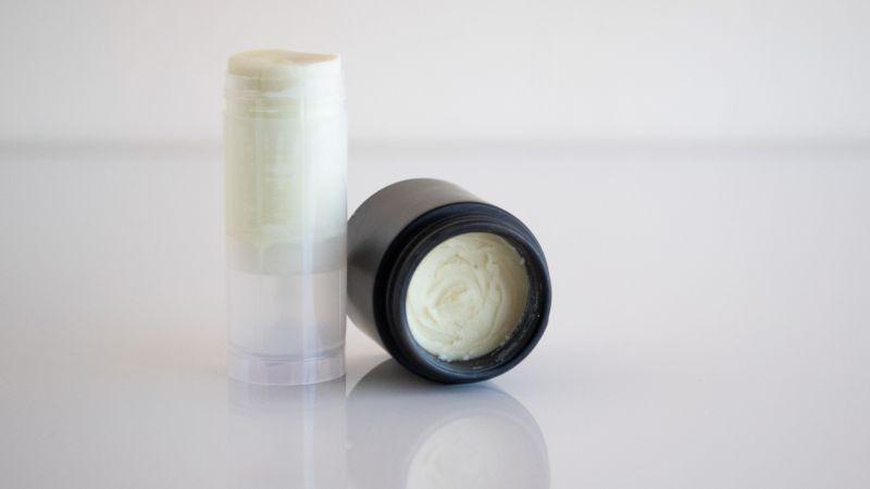 A stick and a small jar of white cream or balm on a white surface.