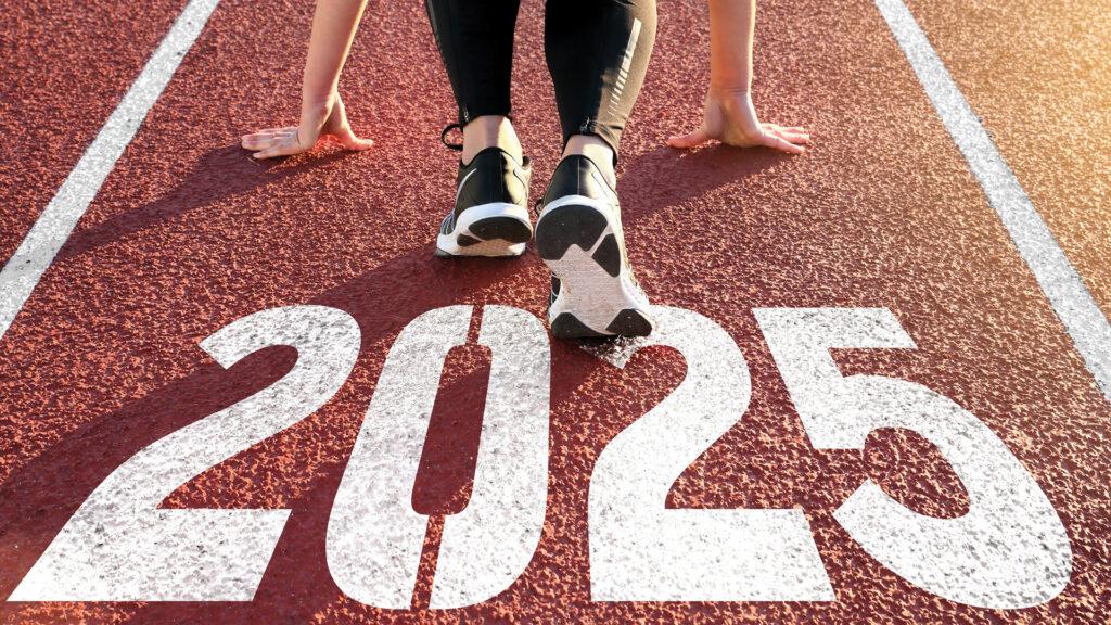 Person in running stance on track with "2025" painted on it, ready to start a race.