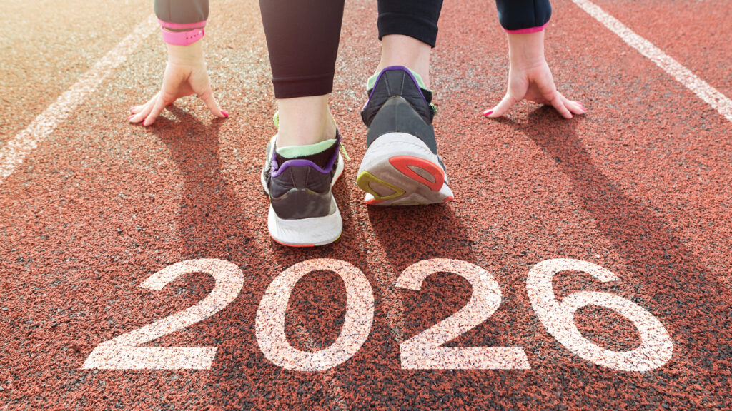 Two runners at the starting line on a track, with "2026" marked on the ground in large white numbers.