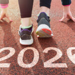 Two runners at the starting line on a track, with "2026" marked on the ground in large white numbers.