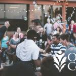 Students gathering outdoors under string lights with "Oakton College" logo in the foreground.