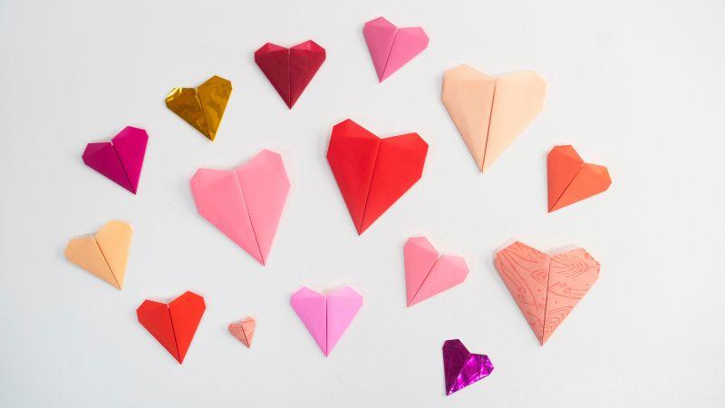 Various colorful origami hearts in red, pink, orange, and gold arranged on a white background.