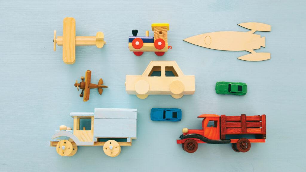 Assorted wooden toy vehicles, planes, and cars arranged neatly on a light blue surface.