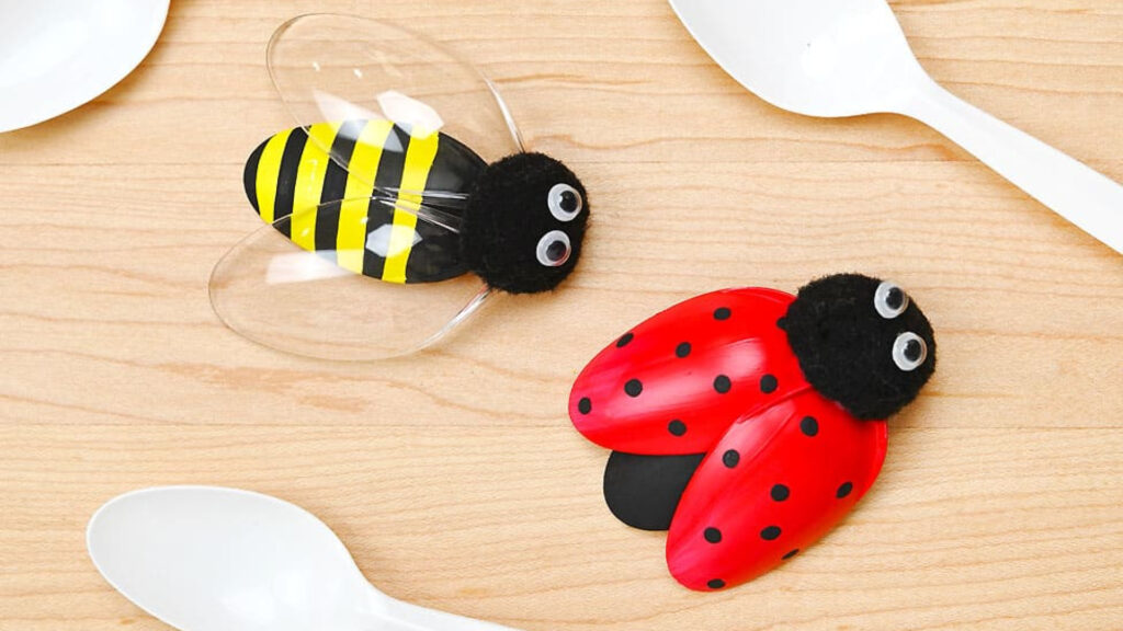 Two plastic spoon crafts: a bee with yellow stripes and a ladybug with red wings and black spots, on a wooden surface.