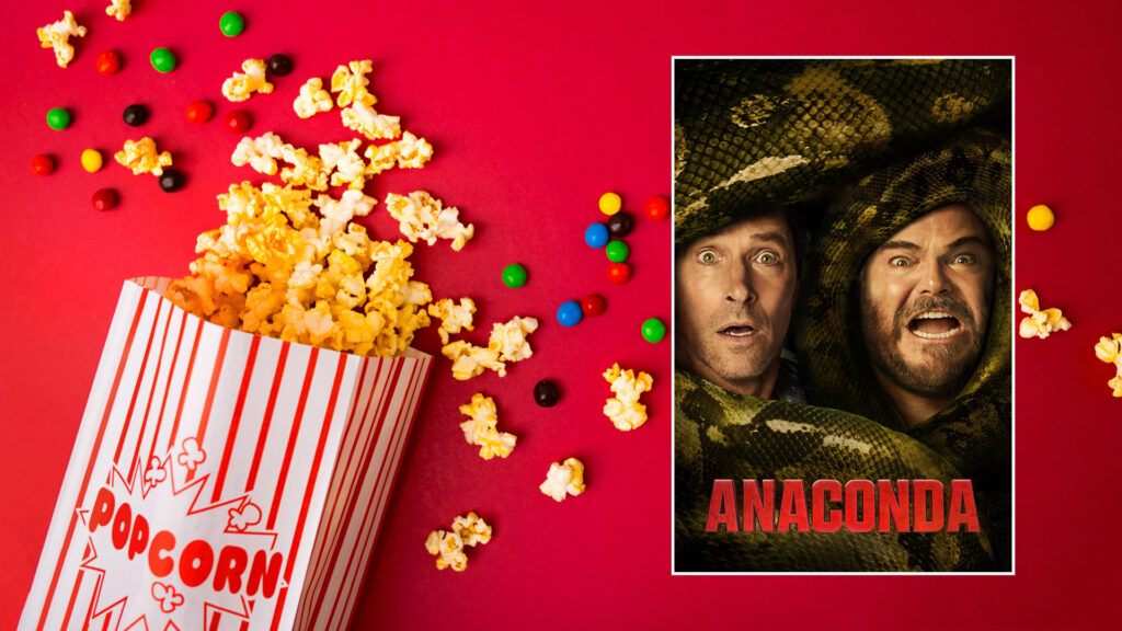 A popcorn box and candy spill on a red surface beside a movie poster for "Anaconda" showing two scared men.