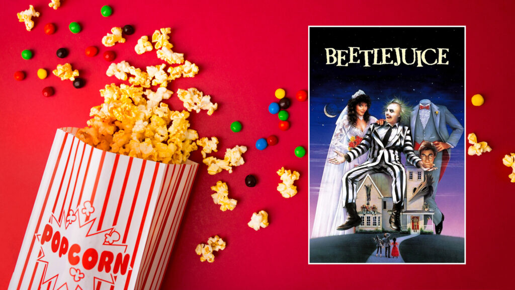 Popcorn and candy spill next to a "Beetlejuice" movie poster on a red background.