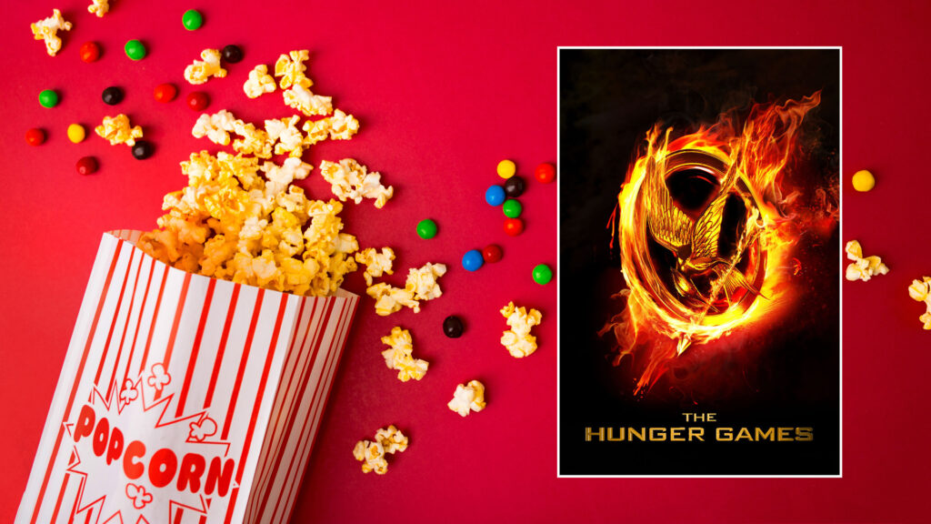 A box of popcorn and candies on a red background next to a "The Hunger Games" movie poster.