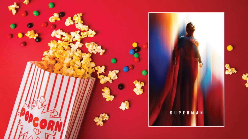 Box of popcorn and colorful candies on a red background next to a Superman movie poster featuring Superman.