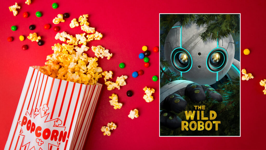 Popcorn and candy spill beside a poster for the movie "The Wild Robot" showing a robot face in foliage.