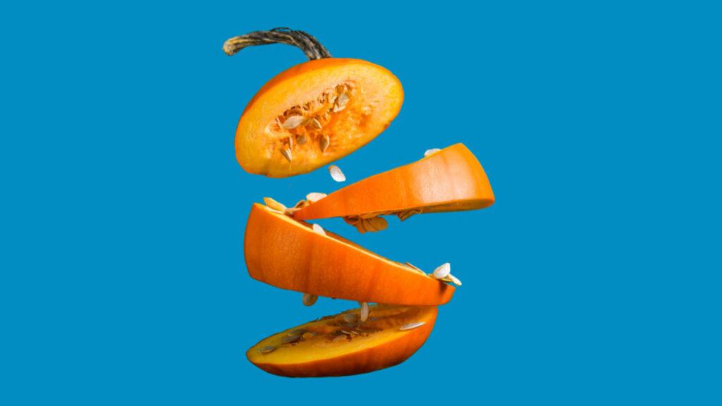 Pumpkin sliced into four floating sections with seeds visible, set against a solid blue background.