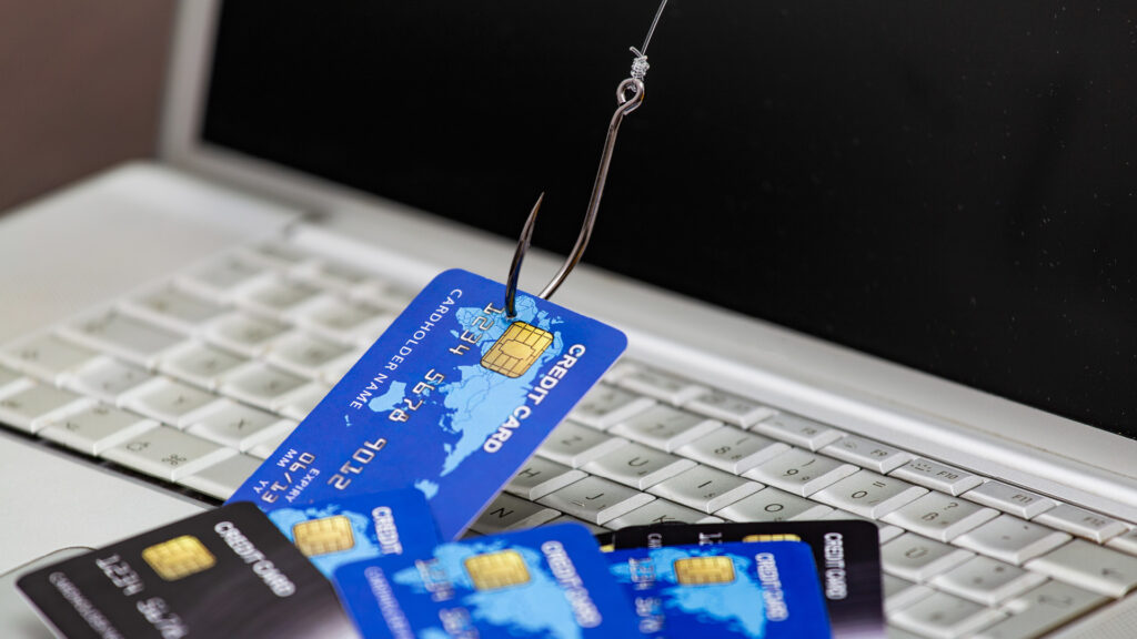 Credit cards hooked on a fishing hook placed on a laptop keyboard, symbolizing phishing and online fraud.