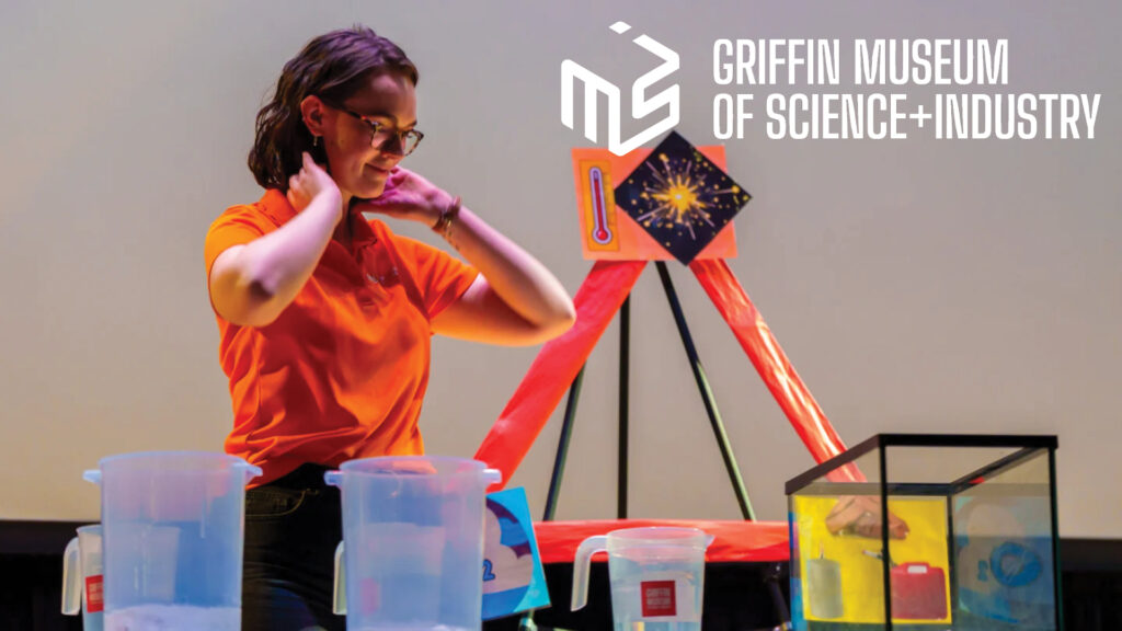 A woman in an orange shirt sets up a science experiment at the Griffin Museum of Science and Industry.