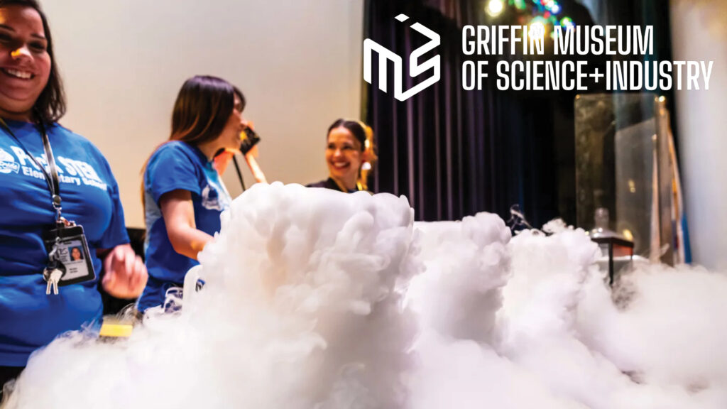Three women stand behind a table with billowing smoke at the Griffin Museum of Science and Industry.