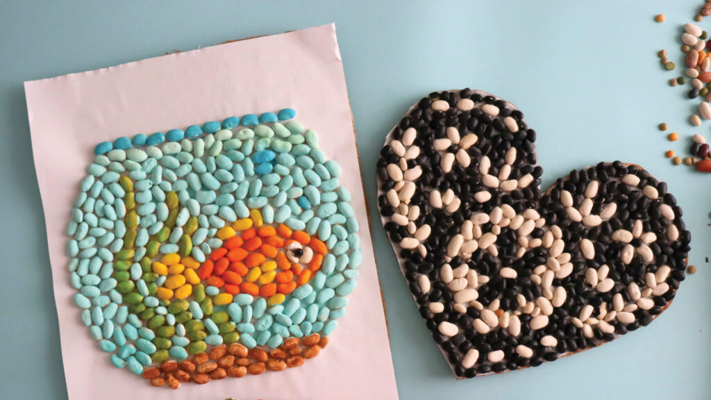 A fishbowl and a heart shape made from colorful beans arranged on a light blue surface.