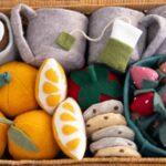 A basket filled with felt toy fruits, tea cups, cookies, and desserts in bright colors.