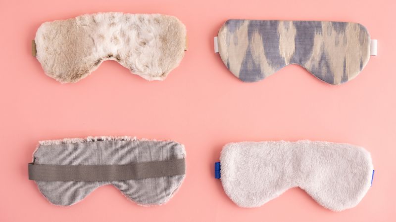 Four sleep masks displayed on a pink background; two are furry and two have fabric patterns.